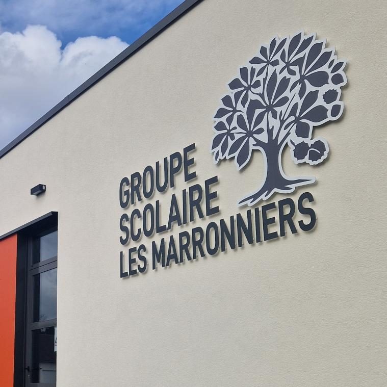 Enseigne du groupe scolaire Les Marronniers, avec lettres en relief et logo d’arbre sur une façade claire.